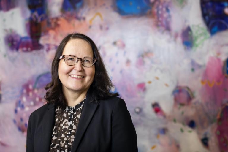 Johanna Osenius kuvattuna värikkään seinän edessä.